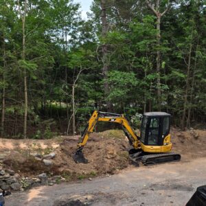 Excavator performing regrading and slope correction on a sloped soil bank in Central Massachusetts