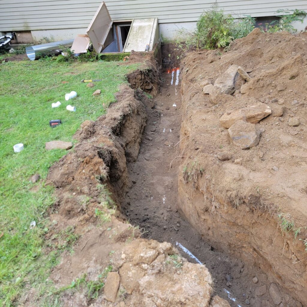 Standing water solutions in Central Massachusetts with a drainage trench beside a home