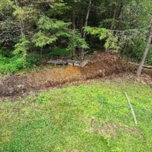 Erosion control shaping bare soil at the base of a wooded slope in Central Massachusetts