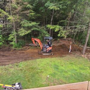 Grading and backfilling reshaping a soil bank above a lawn on a Central Massachusetts property